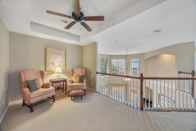 living area featuring a tray ceiling, light colored carpet, visible vents, and baseboards