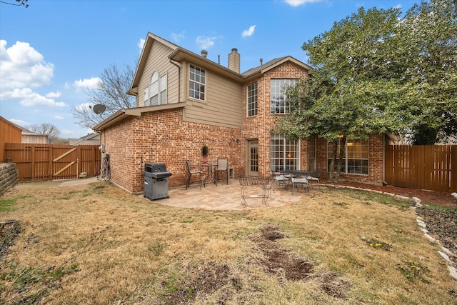 rear view of house with a patio, a fenced backyard, a chimney, a yard, and brick siding