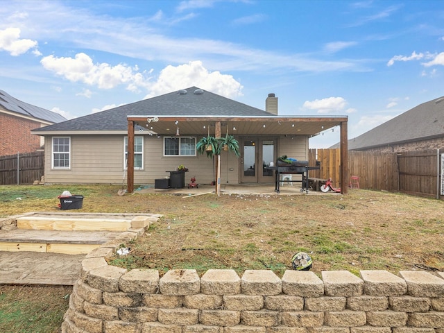 rear view of property with a fenced backyard, french doors, a lawn, a chimney, and a patio area