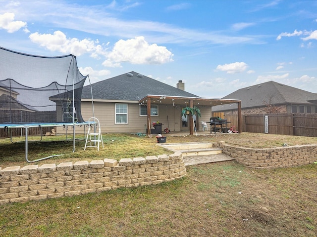 rear view of house featuring a fenced backyard, a trampoline, a yard, a chimney, and a patio area