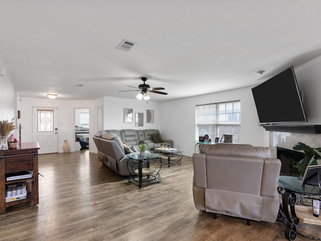 living area featuring ceiling fan, a fireplace, wood finished floors, and visible vents