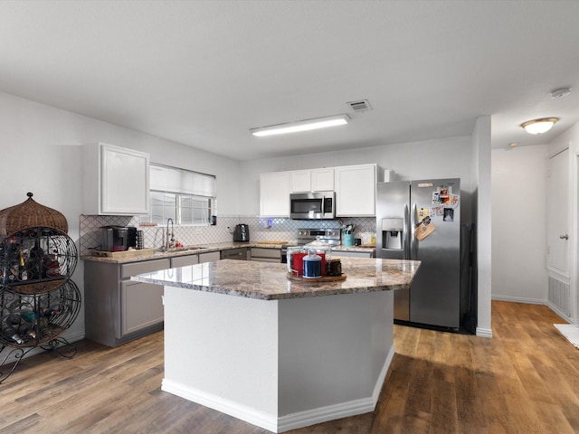 kitchen with a sink, a kitchen island, visible vents, appliances with stainless steel finishes, and dark stone countertops