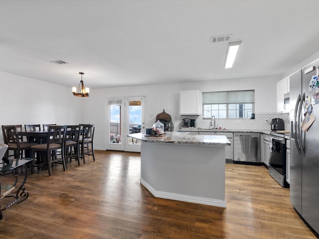 kitchen featuring a center island, decorative light fixtures, stainless steel appliances, visible vents, and white cabinets