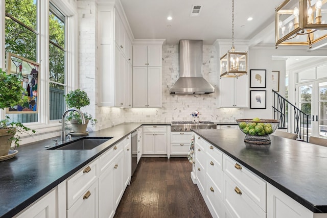 kitchen featuring hanging light fixtures, wall chimney range hood, dark countertops, and a sink