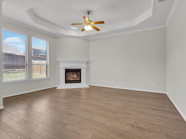 unfurnished living room featuring a tray ceiling, wood finished floors, a glass covered fireplace, and baseboards