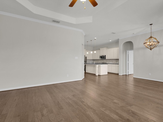 unfurnished living room with arched walkways, a tray ceiling, dark wood finished floors, visible vents, and ceiling fan with notable chandelier