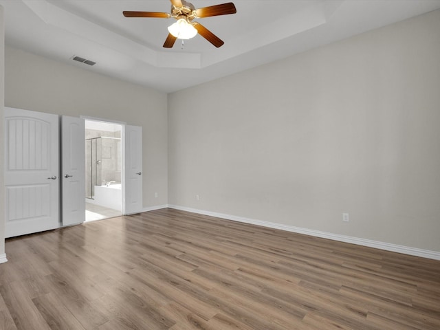 unfurnished room with wood finished floors, a ceiling fan, visible vents, baseboards, and a tray ceiling