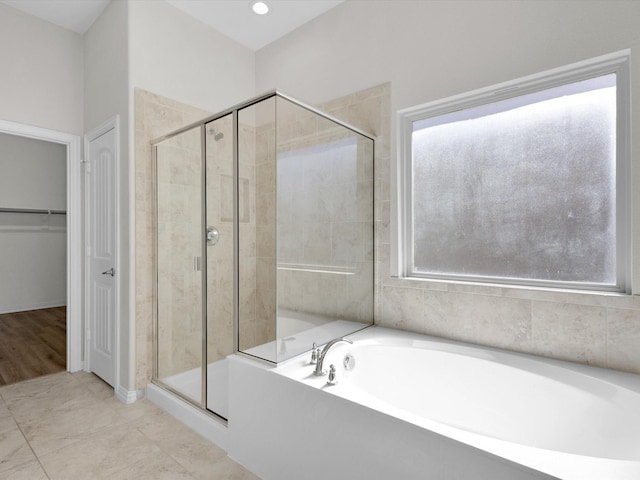 bathroom with a stall shower, a walk in closet, a garden tub, and plenty of natural light