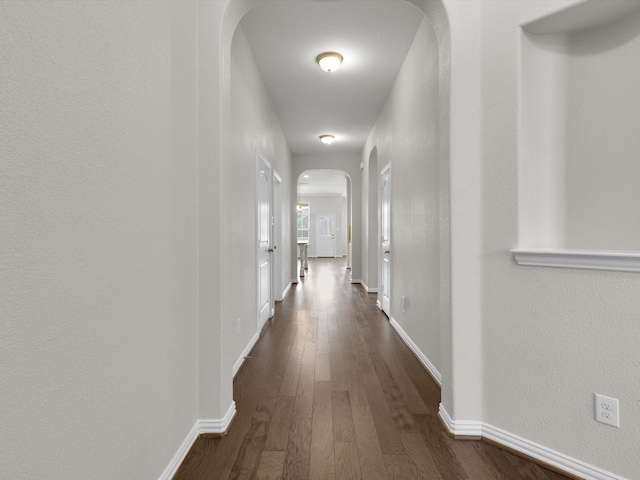 hallway with baseboards, arched walkways, and dark wood-style flooring