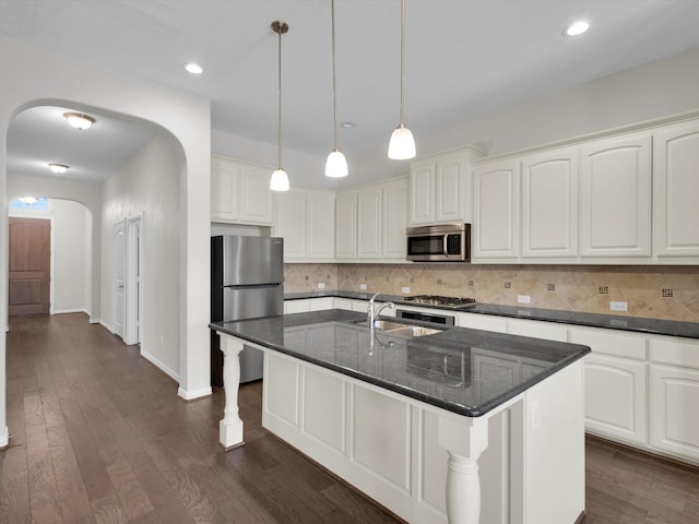 kitchen with arched walkways, dark wood finished floors, decorative backsplash, appliances with stainless steel finishes, and a sink