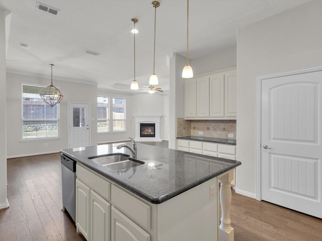 kitchen with a warm lit fireplace, a sink, visible vents, stainless steel dishwasher, and tasteful backsplash