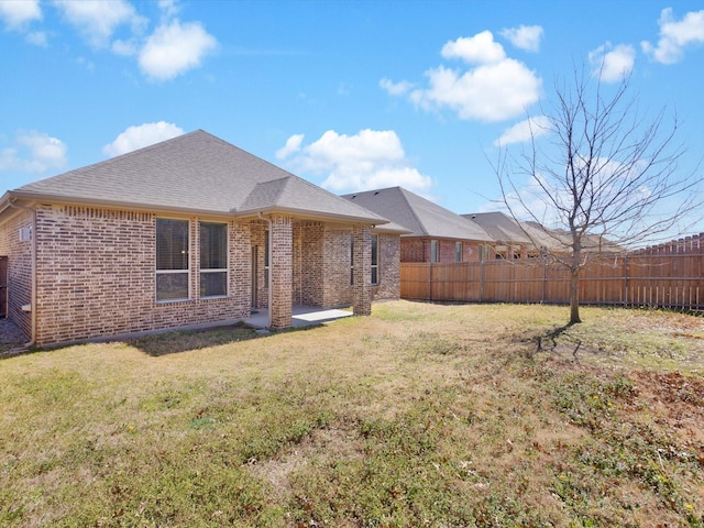 rear view of property featuring a yard, brick siding, fence, and a shingled roof