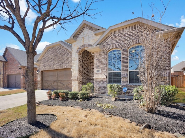 french country home featuring a garage, driveway, brick siding, and fence