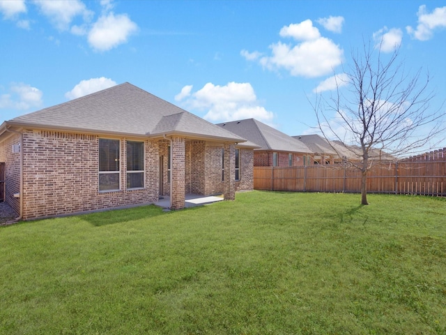 back of property featuring a shingled roof, brick siding, fence, and a lawn