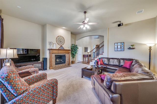 living area with light colored carpet, a fireplace, a ceiling fan, visible vents, and stairway