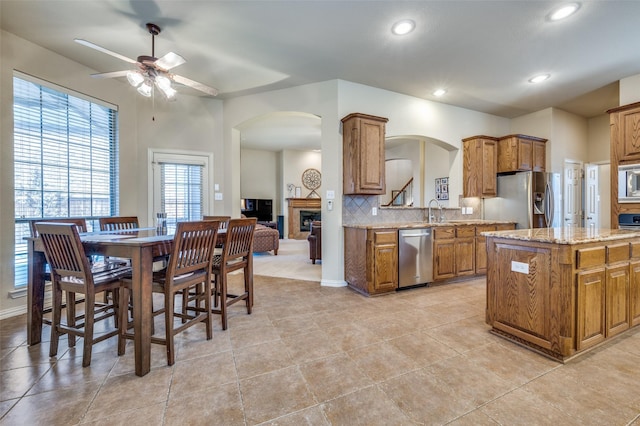 kitchen with light stone counters, a center island, stainless steel appliances, backsplash, and brown cabinetry