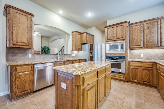 kitchen featuring light tile patterned floors, a kitchen island, light stone counters, brown cabinets, and stainless steel appliances