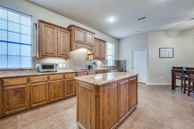 kitchen featuring tasteful backsplash, a toaster, visible vents, brown cabinetry, and a kitchen island