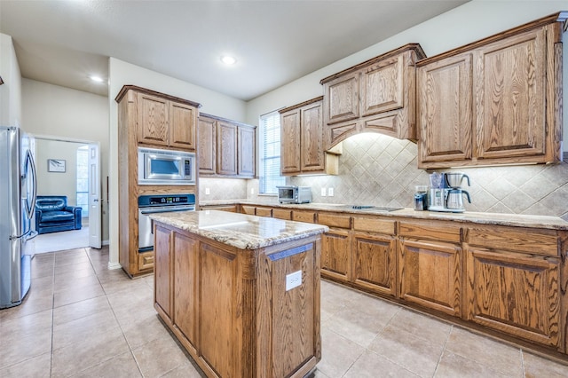 kitchen with light stone countertops, brown cabinetry, stainless steel appliances, and a center island