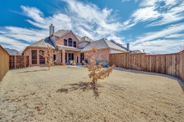 rear view of house featuring a fenced backyard, a chimney, a patio, and brick siding