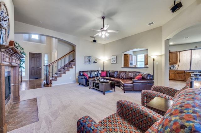 living room featuring baseboards, visible vents, light colored carpet, a fireplace with flush hearth, and stairs