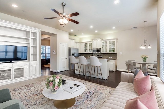 living room with dark wood-style floors, recessed lighting, visible vents, baseboards, and ceiling fan with notable chandelier