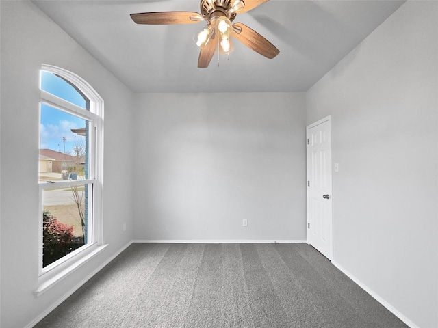 spare room featuring dark colored carpet, ceiling fan, and baseboards