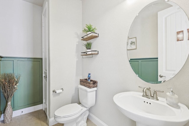 bathroom with a decorative wall, a sink, toilet, and tile patterned floors