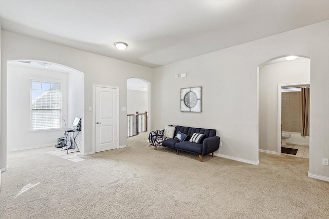 sitting room with arched walkways, baseboards, and light colored carpet