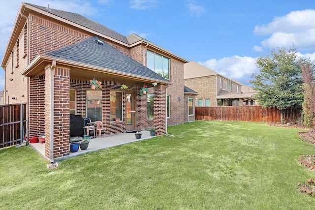 rear view of house with brick siding, roof with shingles, a lawn, a patio area, and a fenced backyard