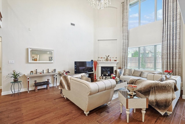 living area with a healthy amount of sunlight, a towering ceiling, wood finished floors, and a glass covered fireplace