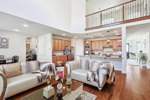 living room with visible vents, arched walkways, dark wood-type flooring, a high ceiling, and recessed lighting