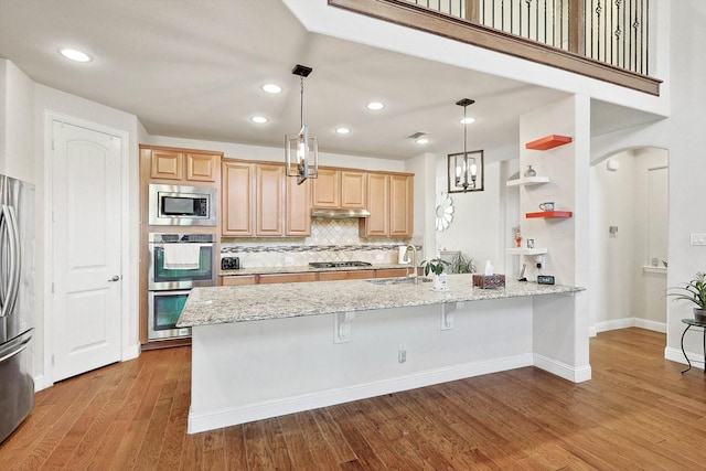 kitchen featuring light stone counters, stainless steel appliances, a sink, and light brown cabinetry