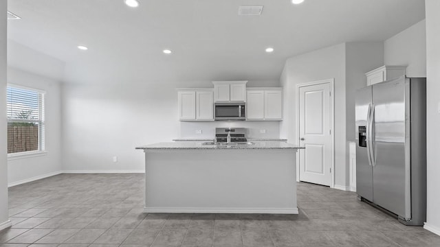 kitchen featuring light stone counters, stainless steel appliances, visible vents, white cabinets, and an island with sink