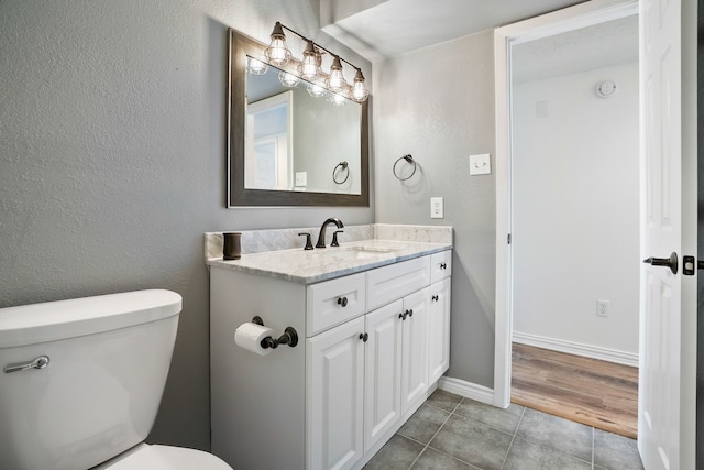 bathroom featuring a textured wall, toilet, vanity, tile patterned flooring, and baseboards