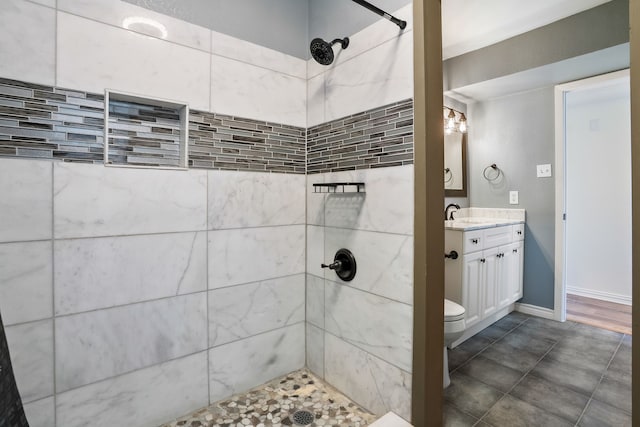 bathroom with toilet, a tile shower, vanity, and baseboards