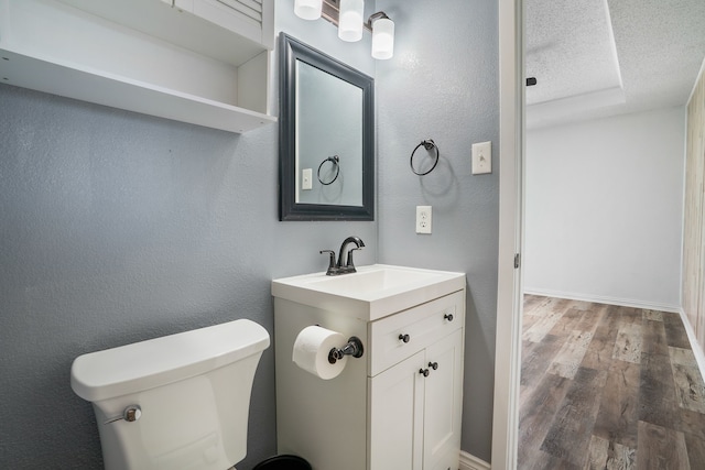 half bathroom featuring a textured ceiling, a textured wall, toilet, wood finished floors, and vanity