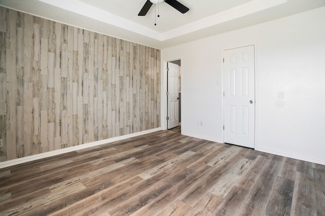 spare room featuring dark wood-type flooring, a tray ceiling, baseboards, and a ceiling fan