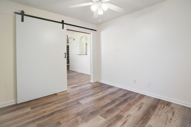 spare room featuring wood finished floors, ceiling fan, baseboards, and a barn door