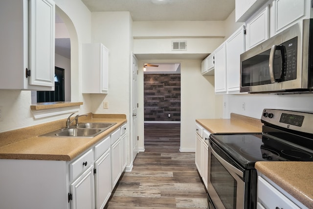 kitchen with dark wood-style flooring, stainless steel appliances, visible vents, white cabinetry, and a sink