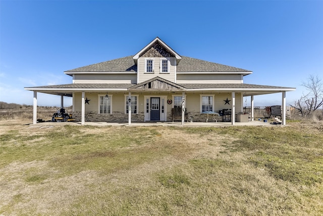 view of front of house with an attached carport, stone siding, roof with shingles, and a front yard