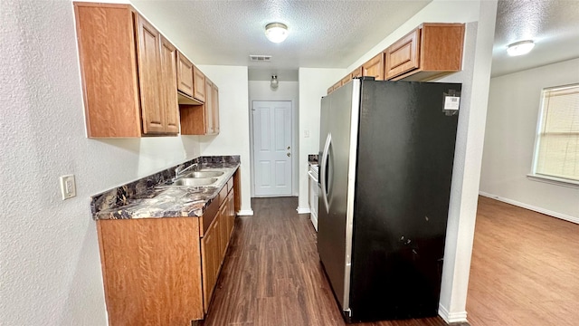 kitchen featuring visible vents, dark wood finished floors, freestanding refrigerator, a textured ceiling, and a sink