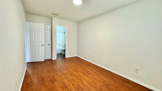 unfurnished bedroom featuring visible vents, connected bathroom, baseboards, and wood finished floors