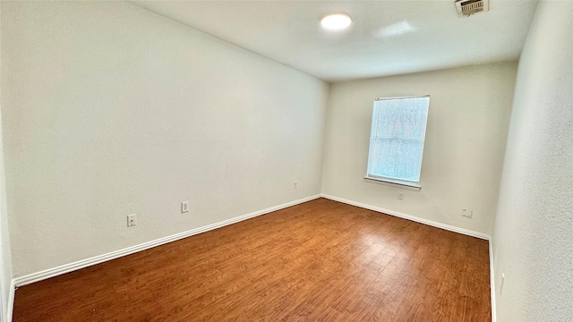 spare room featuring wood finished floors, visible vents, and baseboards