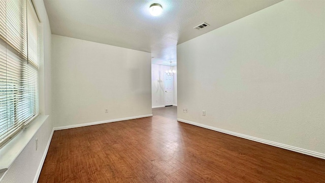 unfurnished room featuring baseboards, visible vents, dark wood-style flooring, a textured ceiling, and a chandelier