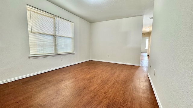 empty room featuring baseboards, wood finished floors, and a textured wall