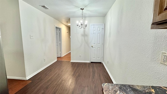 unfurnished dining area with baseboards, visible vents, a textured wall, dark wood-style floors, and a chandelier