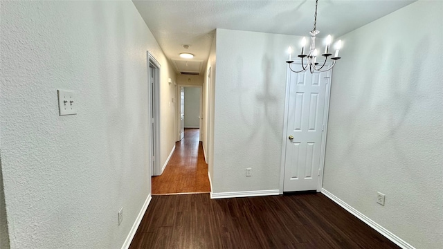 unfurnished dining area with dark wood-type flooring, attic access, a textured wall, and baseboards