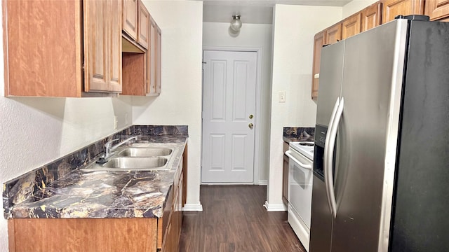 kitchen featuring brown cabinetry, dark stone counters, dark wood-style floors, appliances with stainless steel finishes, and a sink