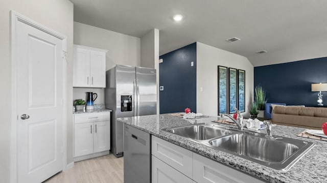 kitchen with white cabinets, light stone counters, appliances with stainless steel finishes, open floor plan, and a sink